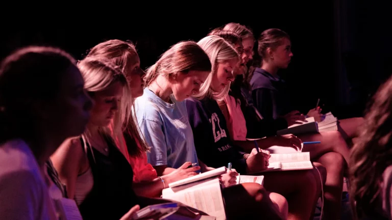 Teenage girls taking notes during a faith-based event at Trinity Baptist Church.