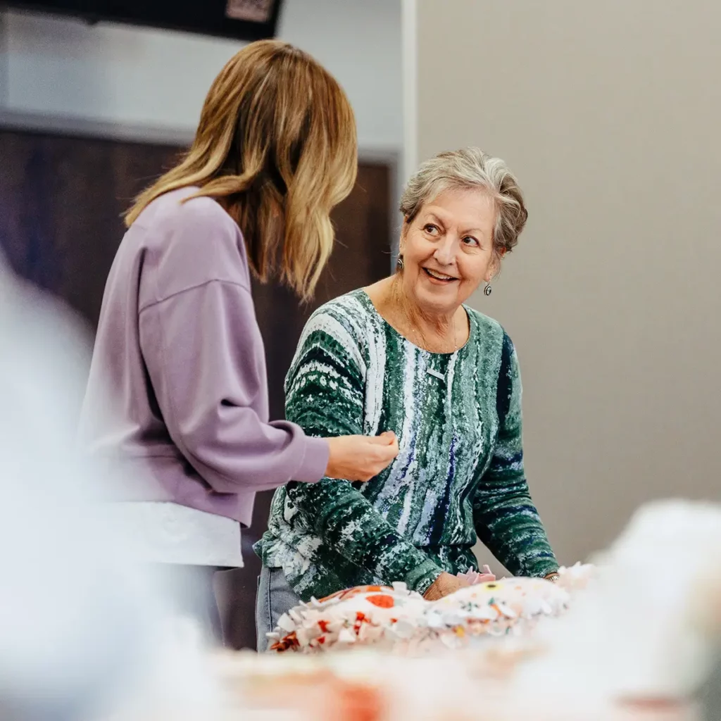 Two women chatting while making fleece blankets during a Trinity Baptist Church service event.