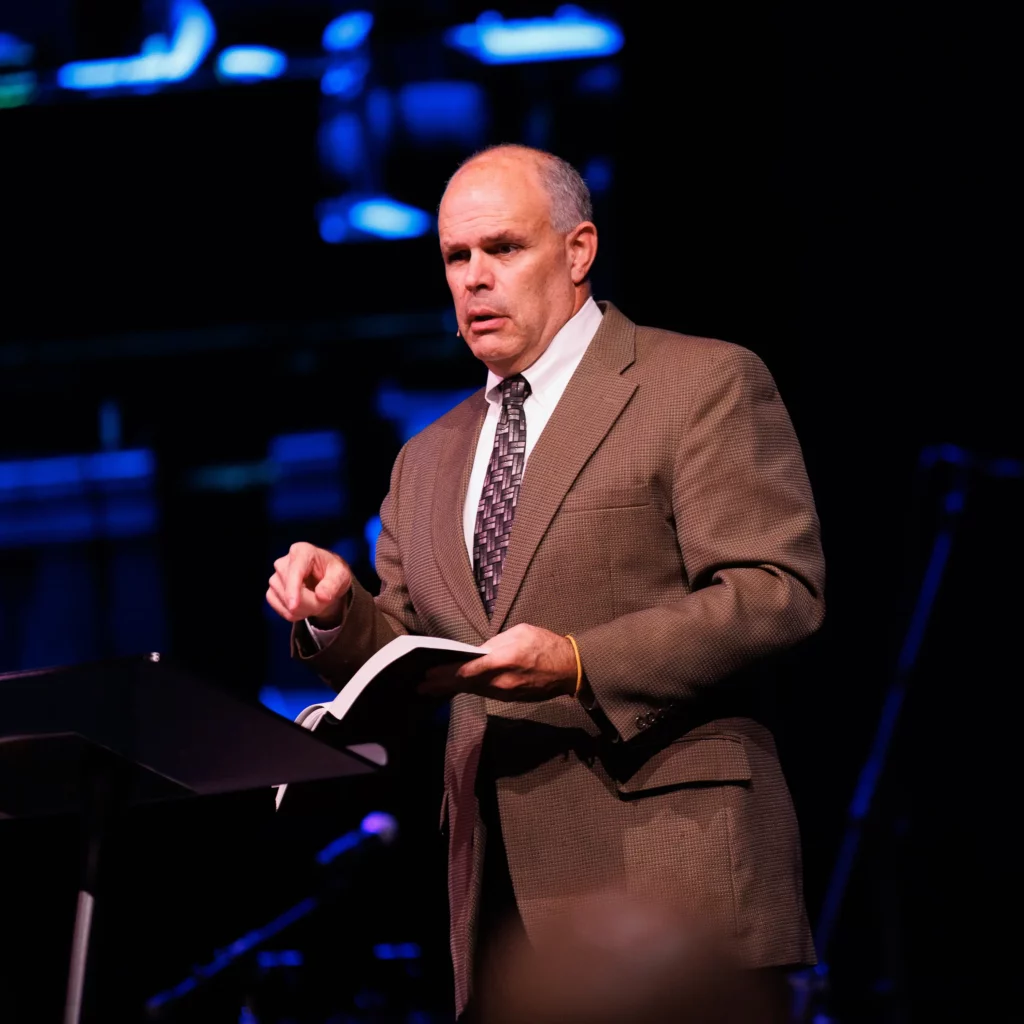 Pastor David Rose preaching from the pulpit with Bible in hand at Trinity Baptist Church.