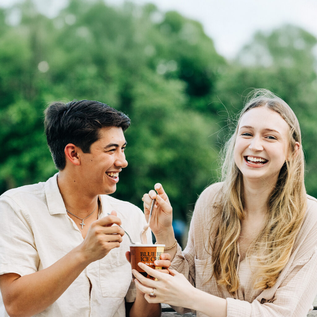 Happy couple laughing and enjoying ice cream together on a park bench