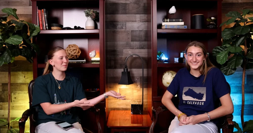 Two young women discuss a mission trip in a podcast studio with bookshelves behind them.