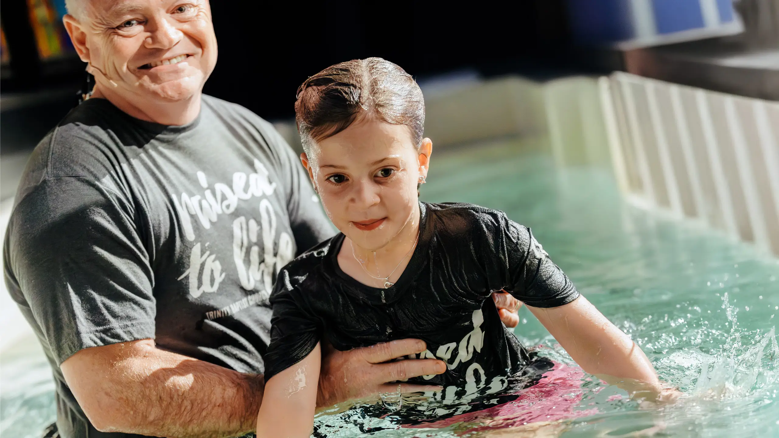 Smiling pastor baptizing young girl at Trinity Baptist Church.