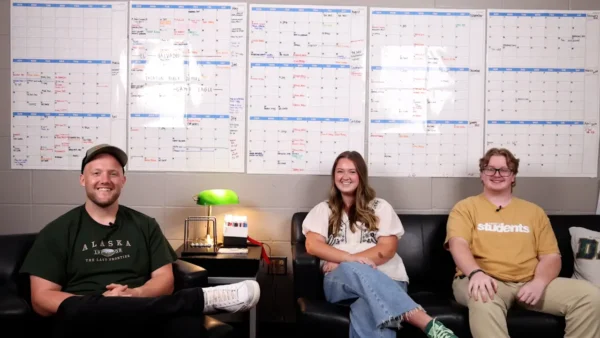 Three student ministry leaders sitting in front of a full ministry calendar wall