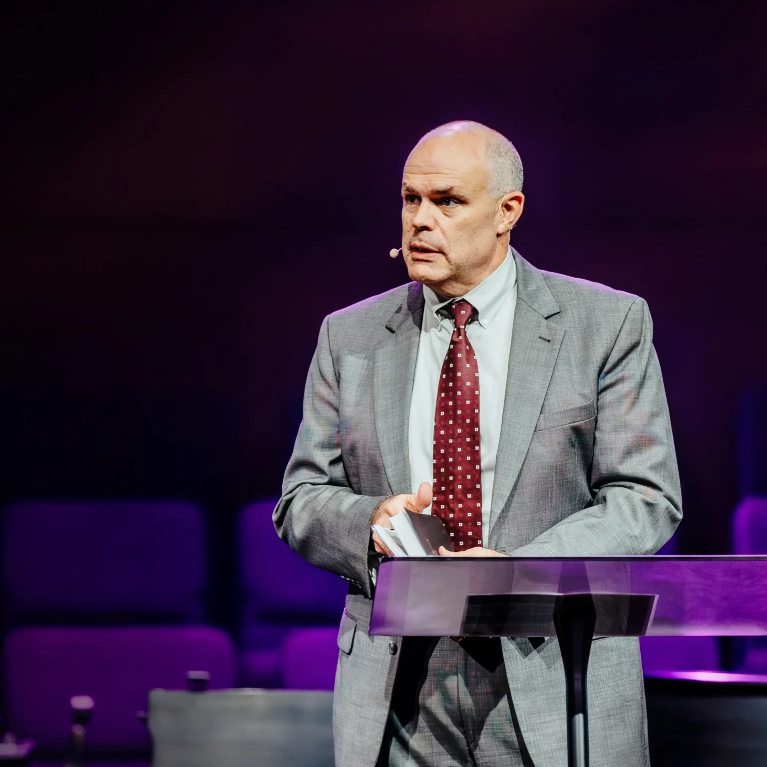 Pastor David Rose speaking at the pulpit in a gray suit during his sermon at Trinity Baptist Church.
