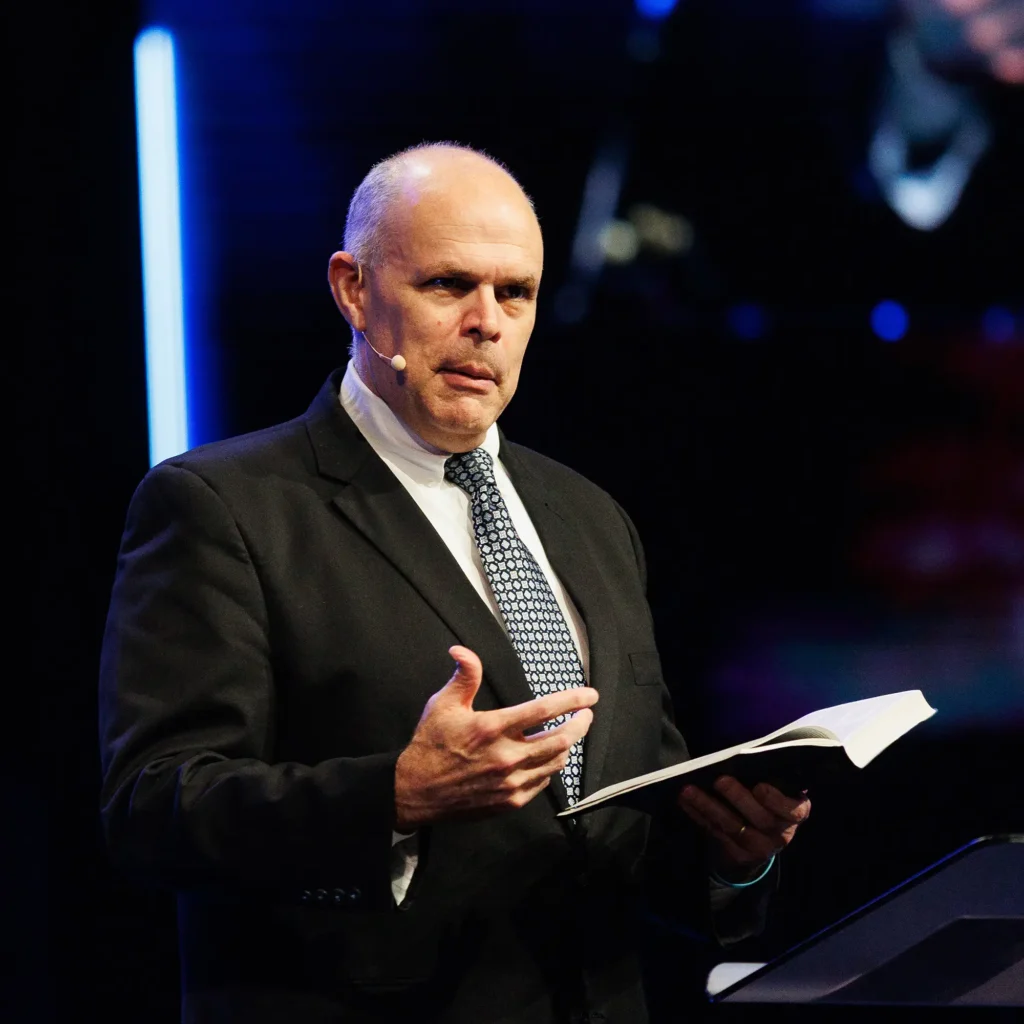 Pastor gesturing while preaching from an open Bible at a church pulpit — Broadening the Tent sermon