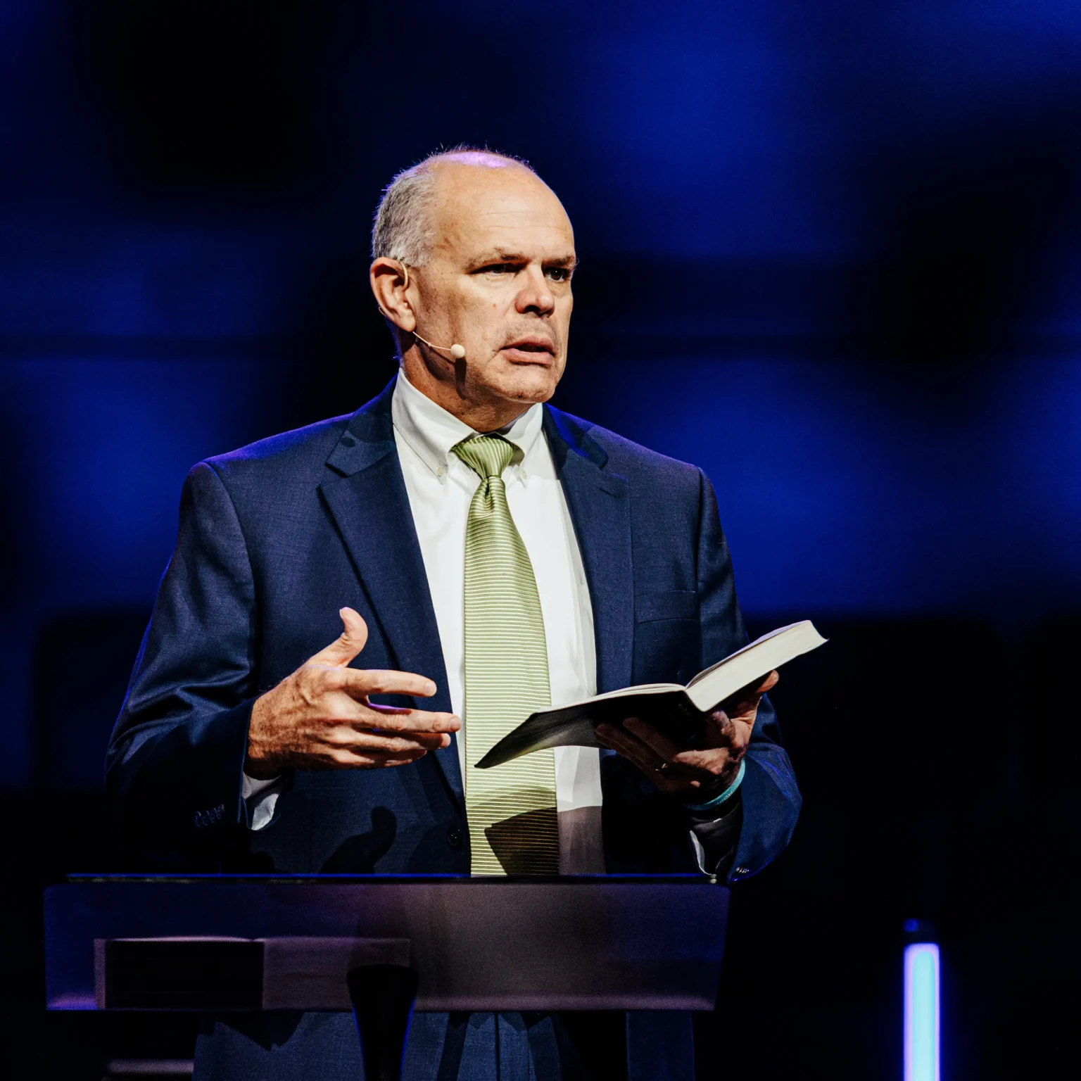 Pastor David Rose delivering a sermon at Trinity Baptist Church in Lake Charles, holding an open Bible on stage.